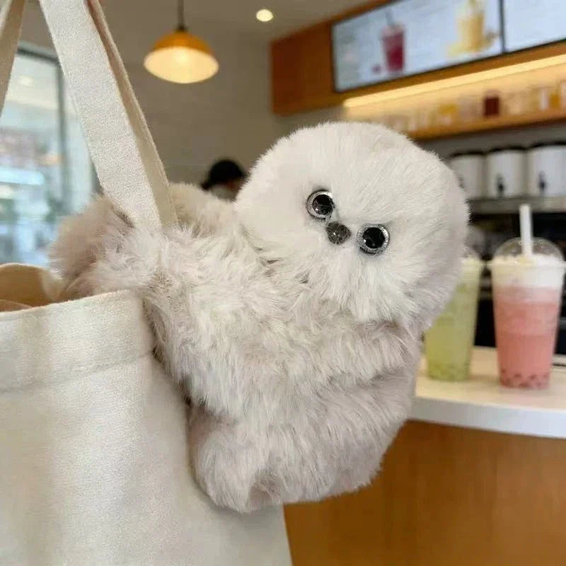 Cream Solis Pip plush companion hooked over the strap of a canvas tote bag in a cafe