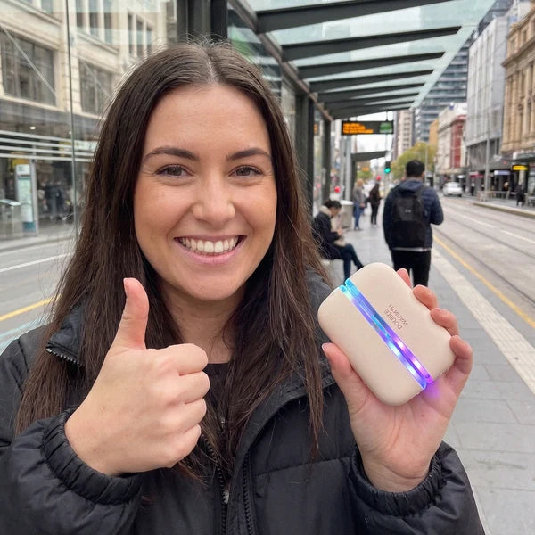 Solis Ember twin hand warmers held in one hand on a city street, the seam lit blue