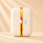 Solis Ember twin hand warmers closed into one ivory pebble, the heating seam glowing amber down the centre