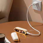Solis Ember twin hand warmers charging from a wall socket by USB-C, the split halves resting on a table beside a coffee