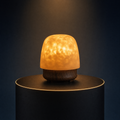 The Solis Lumen ripple lamp on a lit black podium, warm amber light through its textured dome
