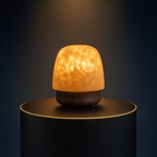 The Solis Lumen ripple lamp on a lit black podium, warm amber light through its textured dome