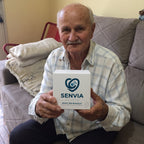 Solis Beacon — elderly man on his sofa holding the SOS bracelet box