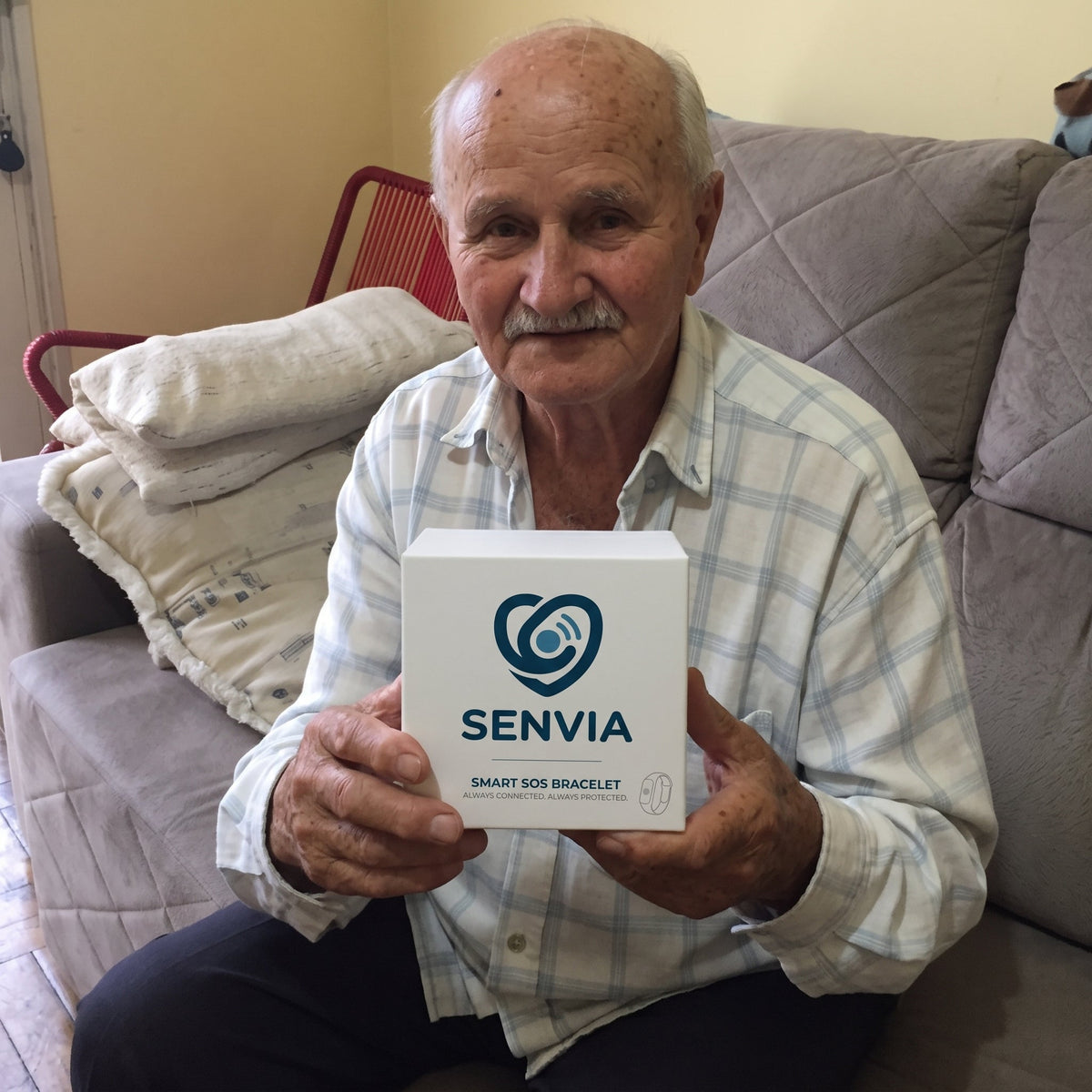 Solis Beacon — elderly man on his sofa holding the SOS bracelet box