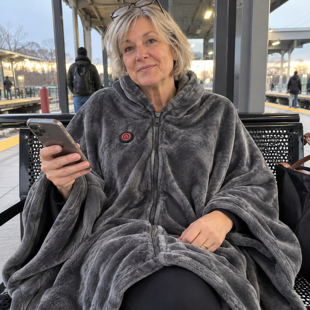 Solis Ember Heated Wearable Blanket in grey worn on a train platform