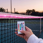 Remote control changing the colour of LED lights on a tennis net at dusk