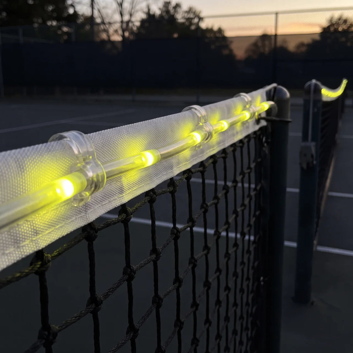 Yellow LED net lights clipped along the top of a tennis net at night